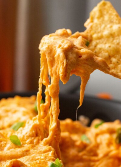 A close up shot of slow cooker buffalo chicken dip scooped up into a tortilla chip.