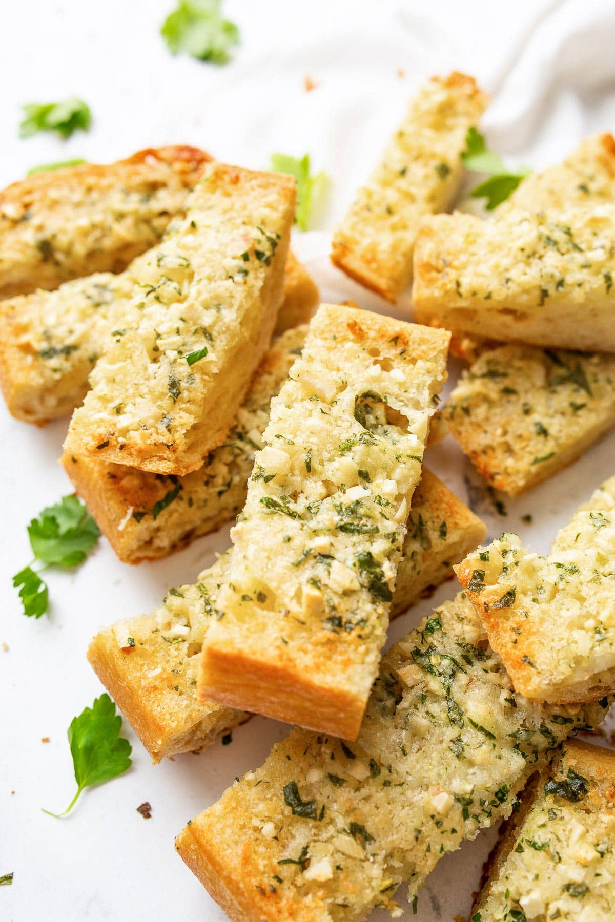 Slices of homemade garlic bread stacked on top of one another and topped with freshly chopped parsley.