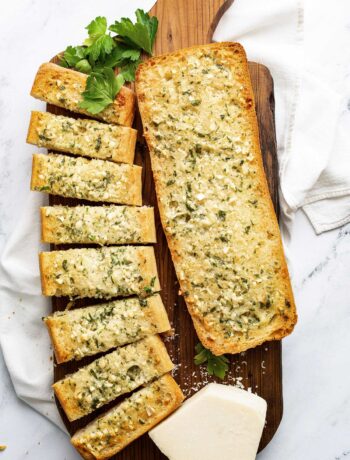 Homemade garlic bread on a cutting board topped with freshly chopped parsley and grated cheese.