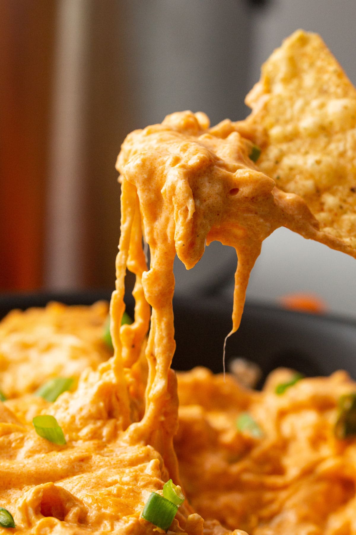 A close-up of a slow-cooking buffalo chicken dip added into a tortilla chip.