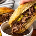 A slow cooker Italian beef sandwich being dipped into a bowl of au jus.