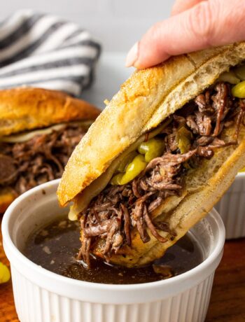 A slow cooker Italian beef sandwich being dipped into a bowl of au jus.