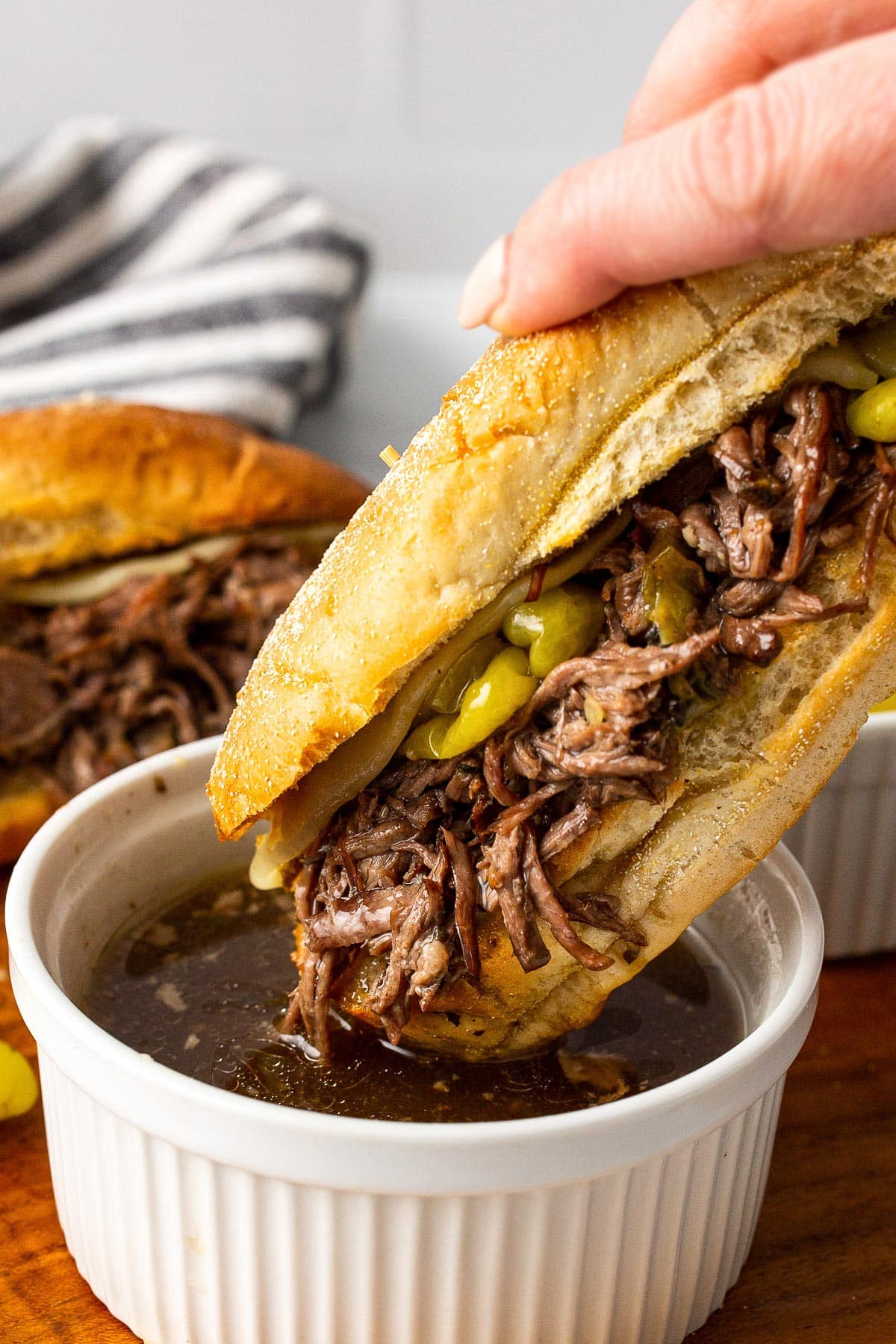 A slow cooker Italian beef sandwich being dipped into a bowl of au jus.