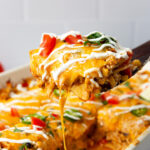 A hearty slice of chicken enchilada casserole lifted out of a white 9x13 casserole pan.