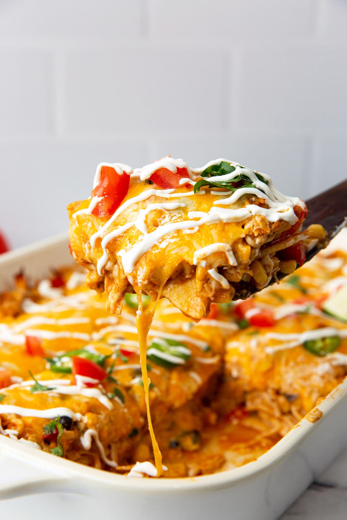 A hearty slice of chicken enchilada casserole lifted out of a white 9x13 casserole pan.