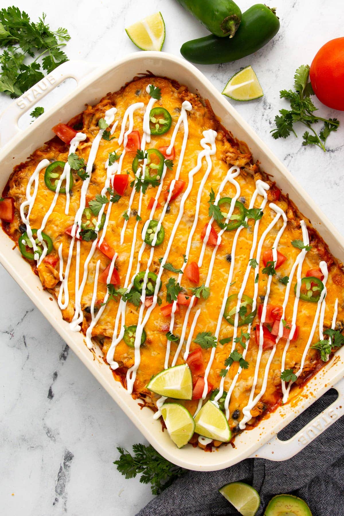 A top down shot of chicken enchilada casserole in a white 9x13 casserole pan topped with jalapeno, green onions, tomatoes and sour cream.