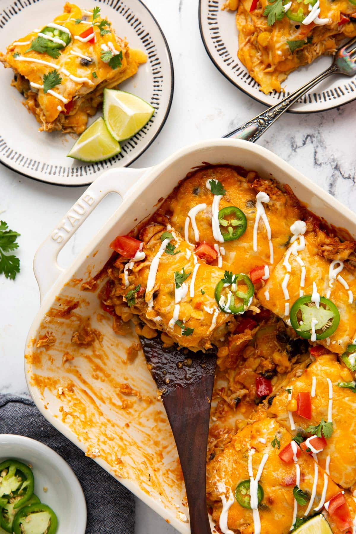 A top down shot of chicken enchilada casserole in a white 9x13 casserole with two slices off the side in serving plates.