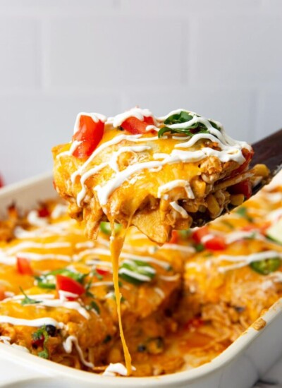 A hearty slice of chicken enchilada casserole lifted out of a white 9x13 casserole pan.