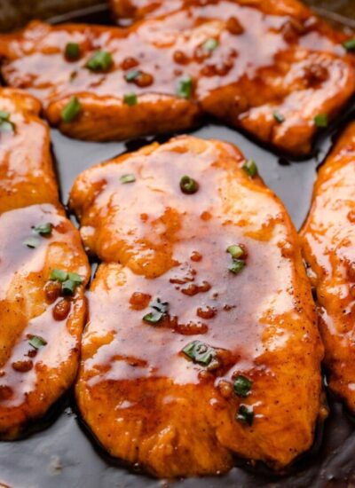 Honey garlic butter chicken breasts smothered in sauce and topped with green onions in a stainless steel skillet.