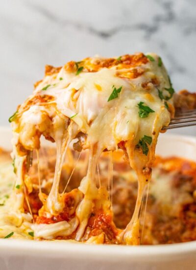 A portion of ravioli lasagna bake lifted from the casserole dish with lots of cheese strings.