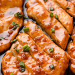 Honey garlic butter chicken breasts smothered in sauce and topped with green onions in a stainless steel skillet.