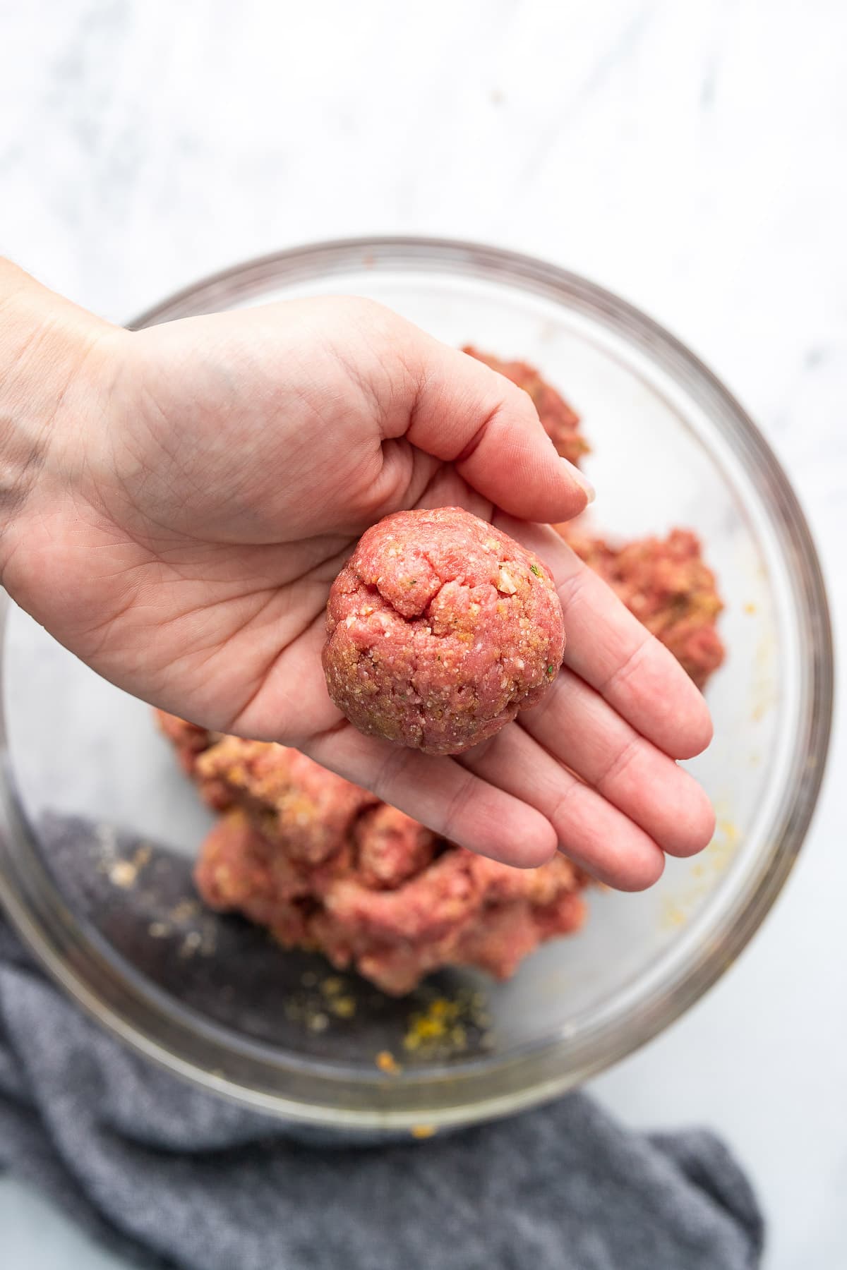 A hand holding a single freshly formed Parmesan meatball.