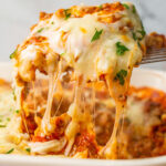 A portion of ravioli lasagna bake lifted from the casserole dish with lots of cheese strings.