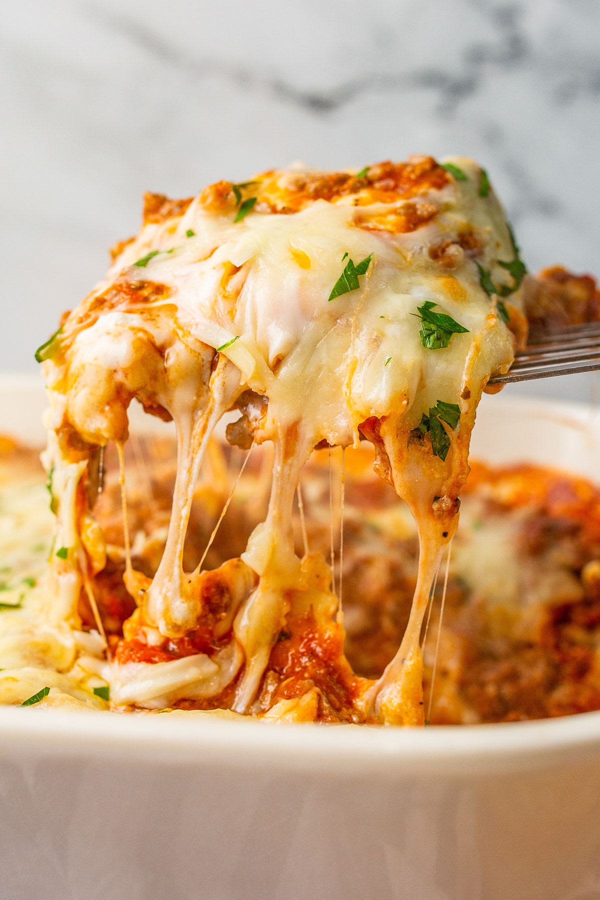 A portion of ravioli lasagna bake lifted from the casserole dish with lots of cheese strings.