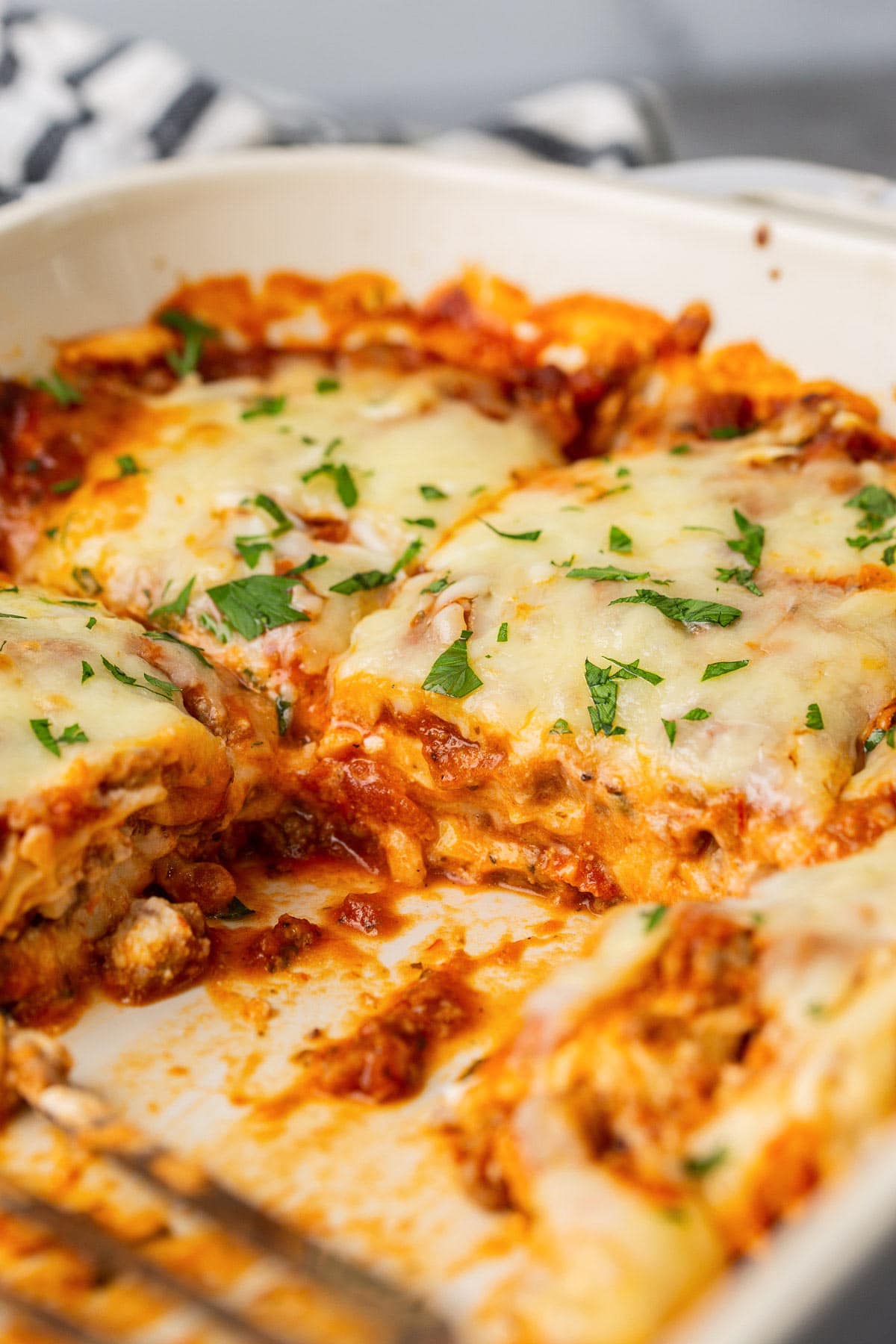 Ravioli lasagna bake in a white 9x13 casserole dish topped with freshly chopped parsley.