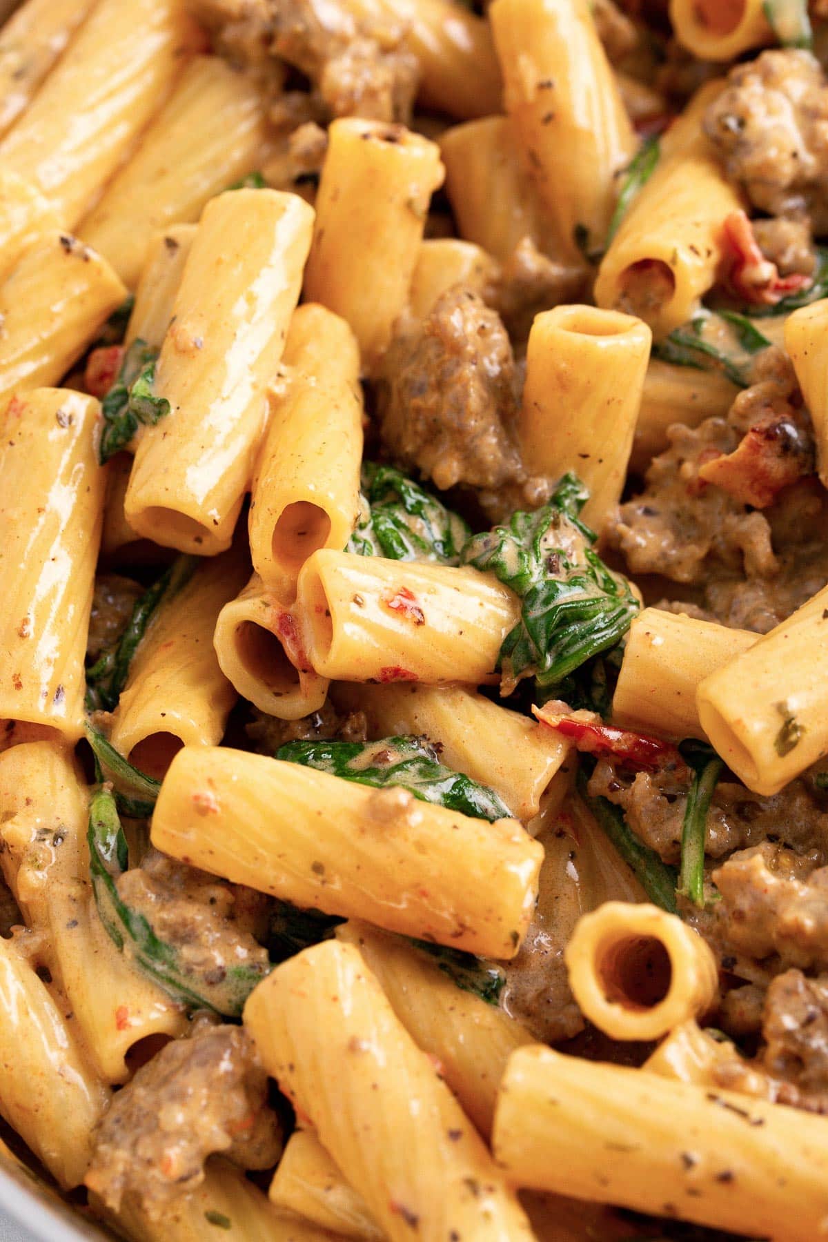 A close up shot of Tuscan sausage pasta with rigatoni, Italian sausage, spinach and sun-dried tomatoes smothered in a cream sauce.
