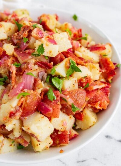 German potato salad in a white bowl topped with freshly chopped parsley.