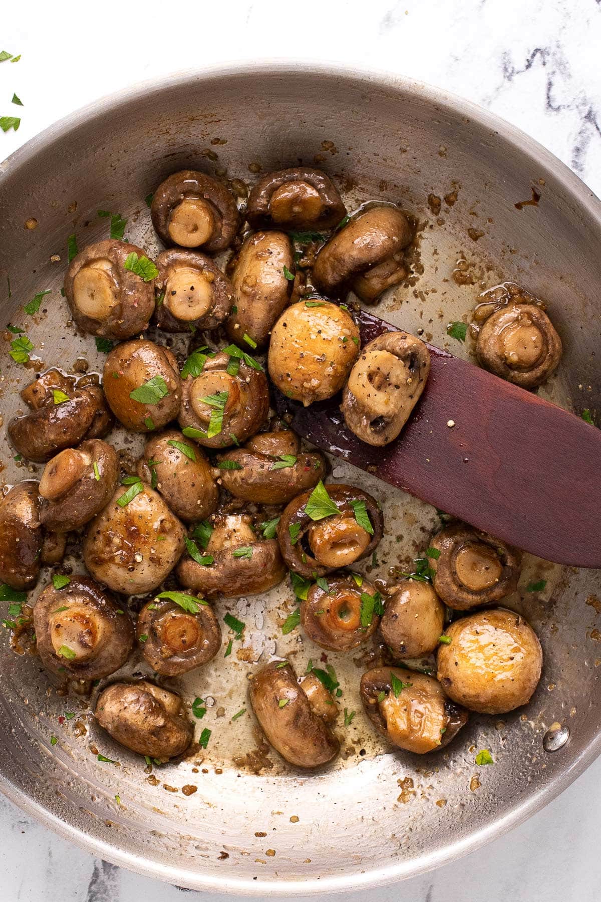 Some garlic butter mushrooms sauteeing in a stainless steel skillet topped with freshly chopped parsley.