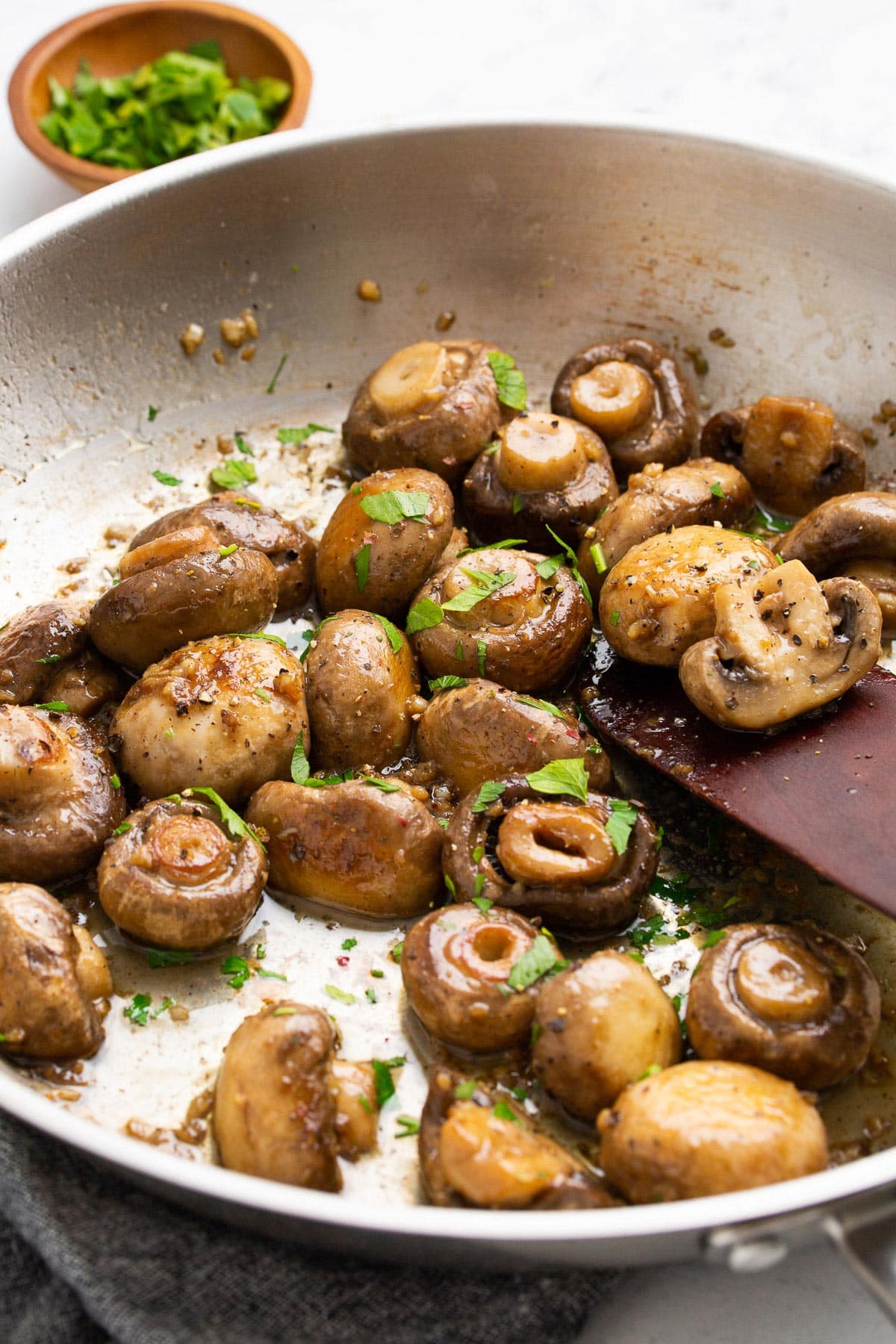 Some garlic butter mushrooms sauteeing in a stainless steel skillet topped with freshly chopped parsley.