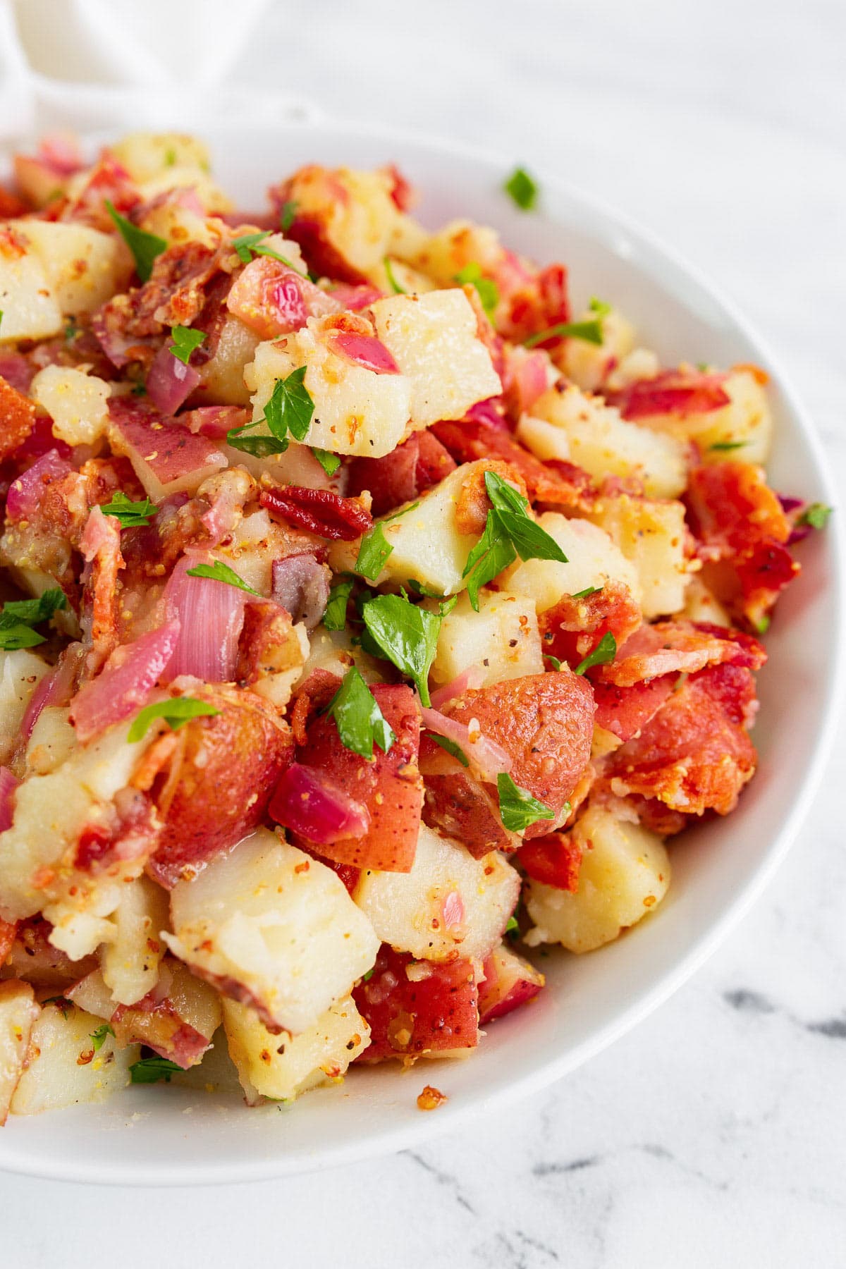 German potato salad in a white bowl topped with freshly chopped parsley.