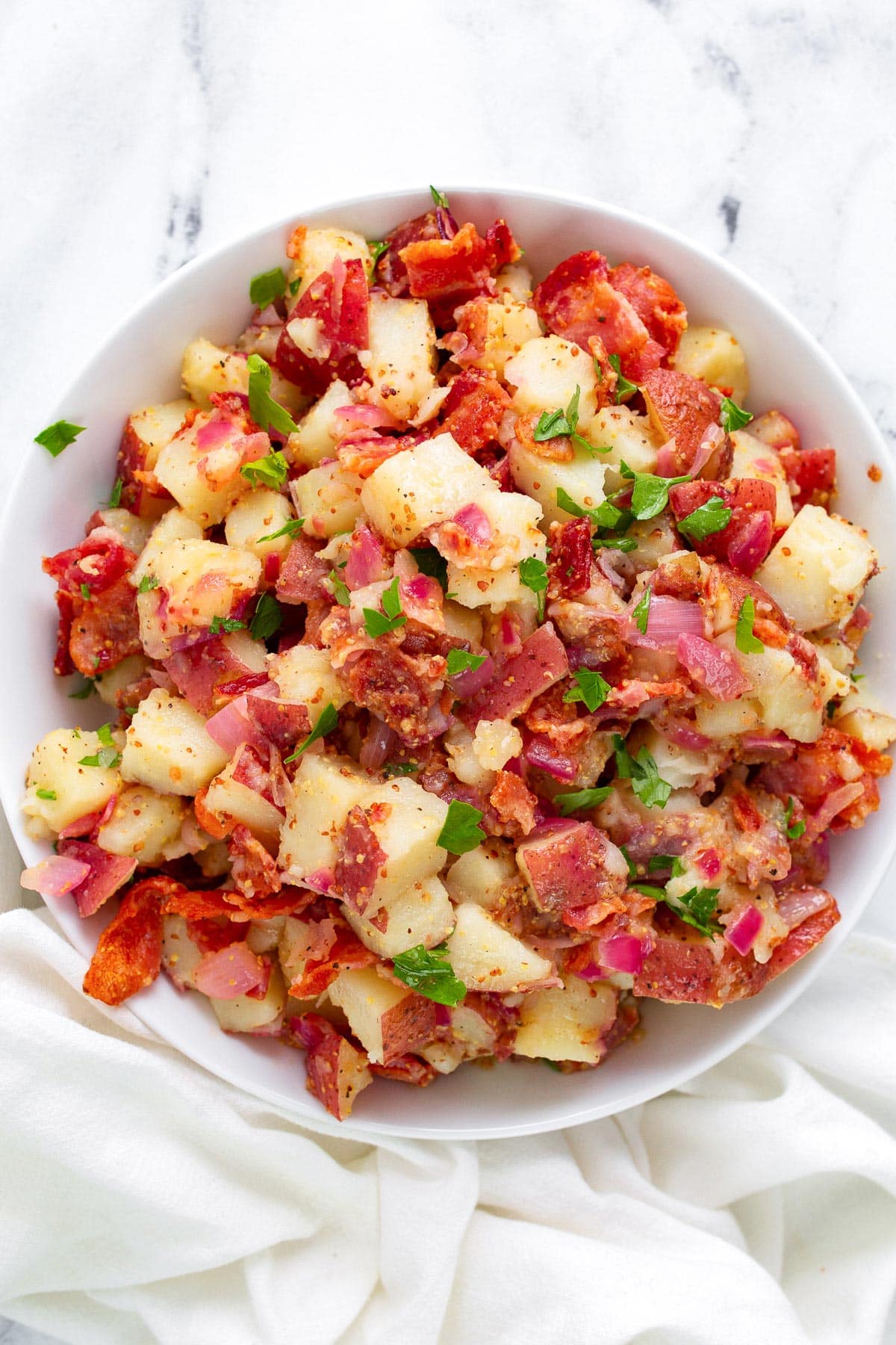 German potato salad in a white bowl topped with freshly chopped parsley.