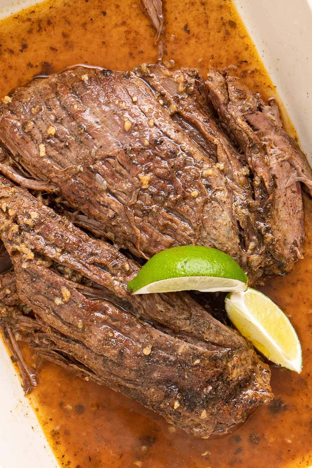 Slow cooker carne asada swimming in its juices and topped with two lime wedges.
