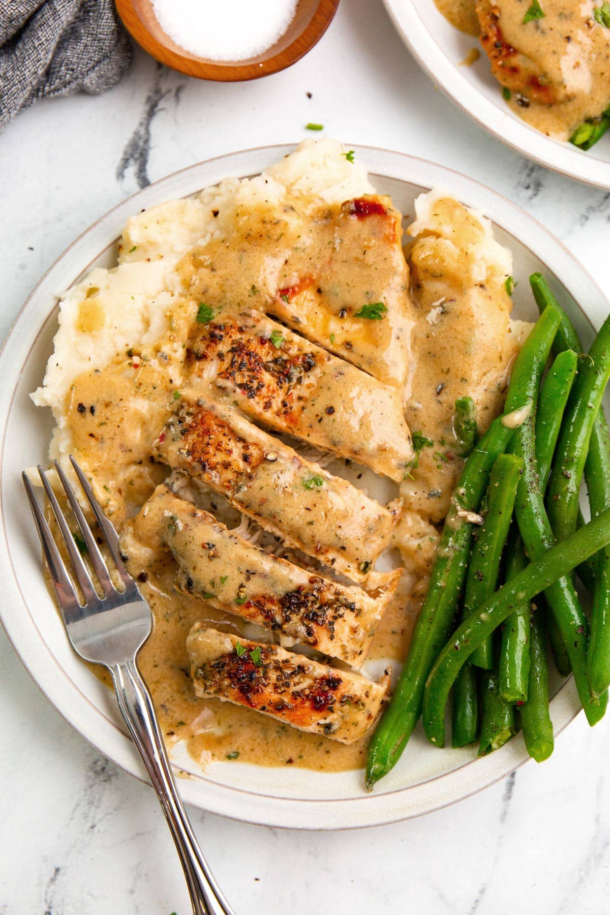 Creamy ranch chicken on a white plate over mashed potatoes and a side of green beans.