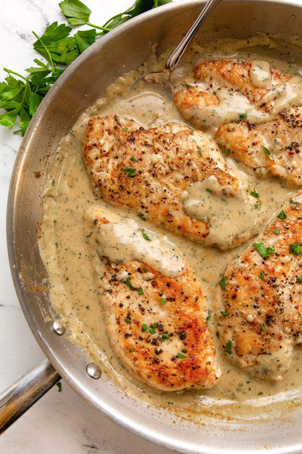 Creamy ranch chicken in a stainless steel skillet smothered in sauce and topped with chopped fresh parsley.