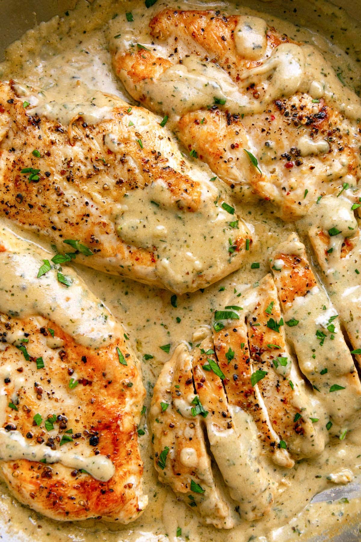 Creamy ranch chicken in a stainless steel skillet smothered in sauce and topped with chopped fresh parsley.