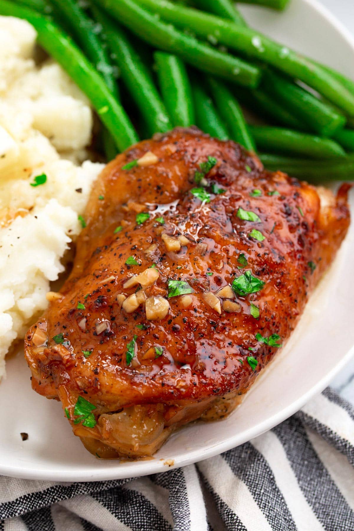 Brown sugar garlic chicken on a white plate served with mashed potatoes and green beans.