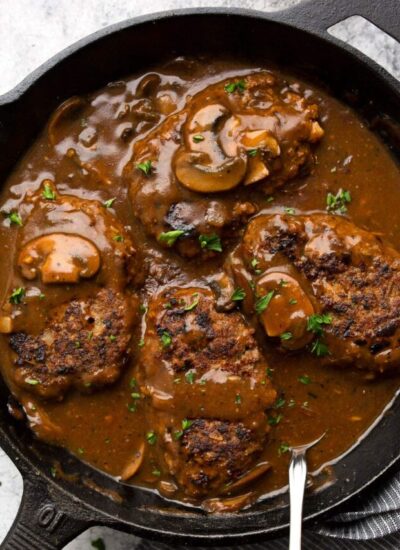 Salisbury steak in a cast iron pan smothered in a mushroom gravy and topped with chopped fresh parsley.