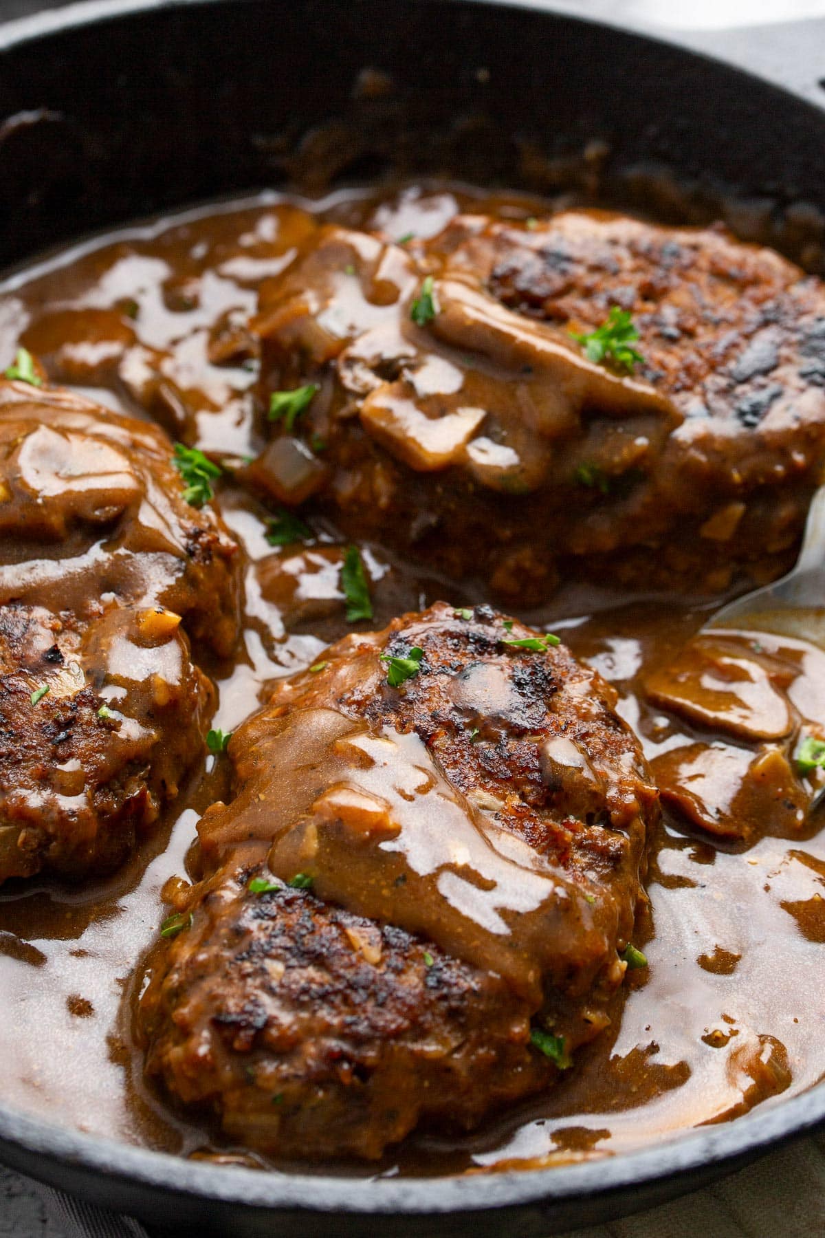 Salisbury steak in a cast iron pan smothered in a mushroom gravy and topped with chopped fresh parsley.