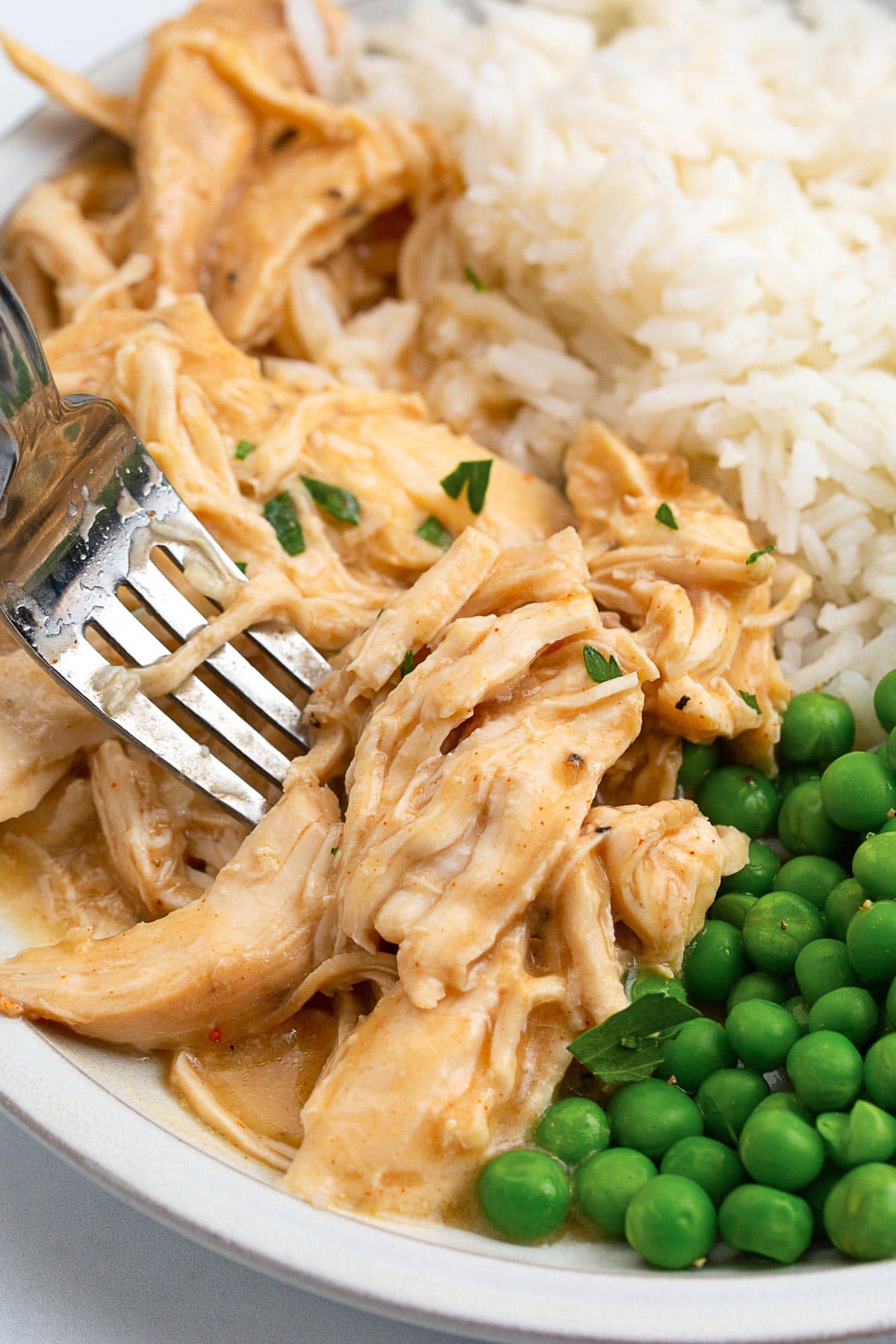Slow cooker chicken and gravy on a plate with white rice and green peas.