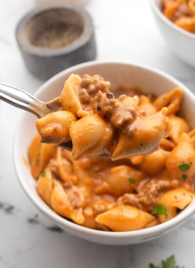 A generous serving of creamy beef and shells on a spoon with two bowls of it in the background.