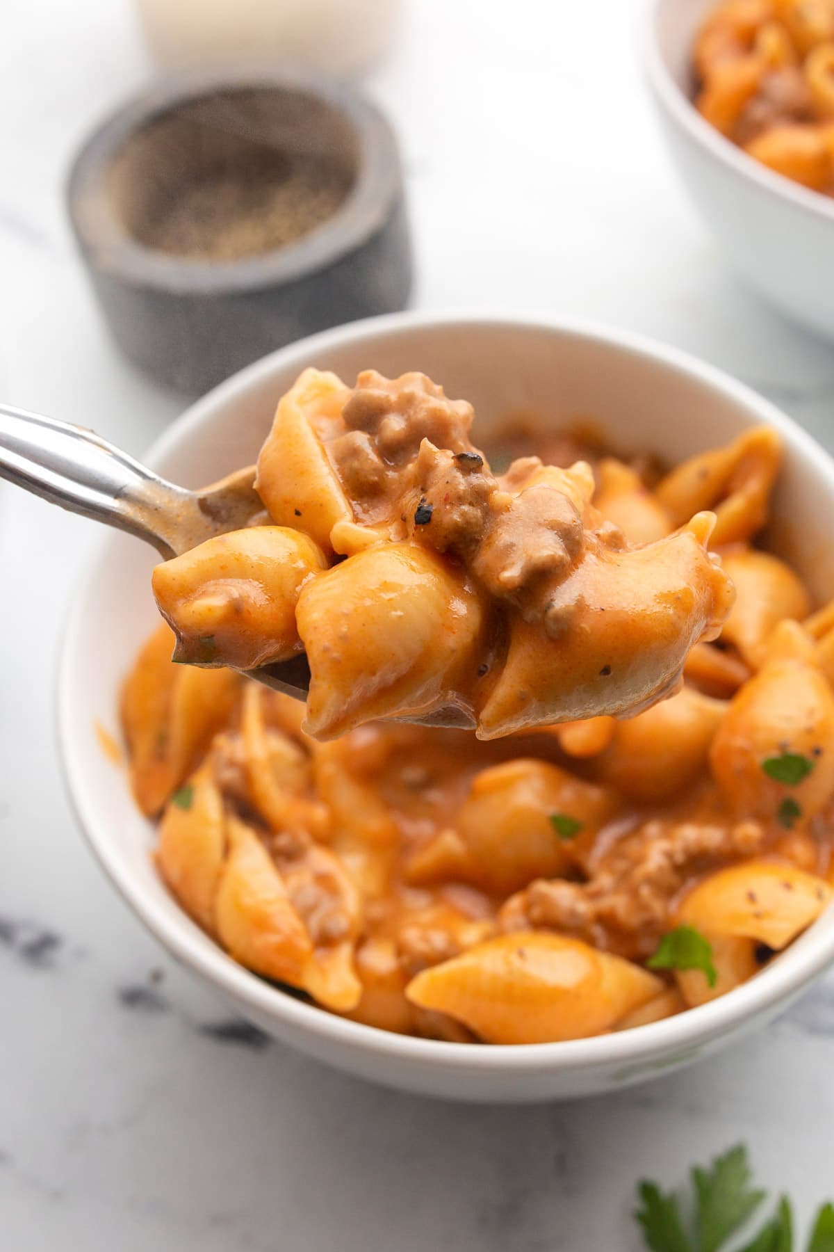 A generous serving of creamy beef and shells on a spoon with two bowls of it in the background.