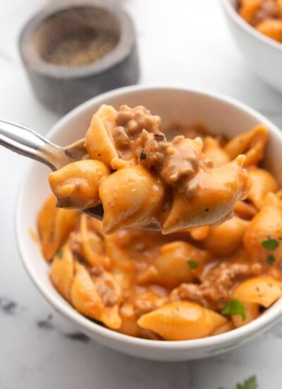 A generous serving of creamy beef and shells on a spoon with two bowls of it in the background.