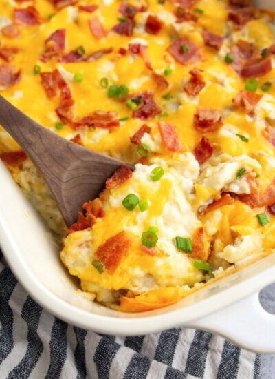 A close up shot of twice baked potato casserole topped with cheese, bacon bits and green onions.