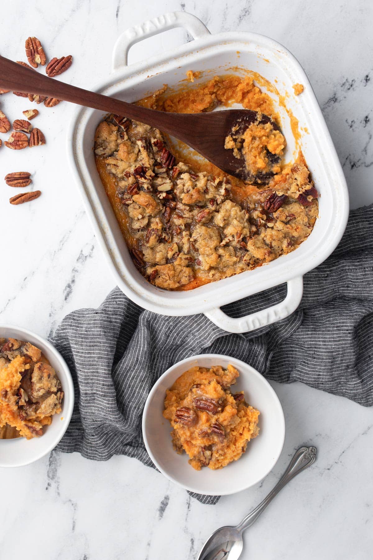 Sweet potato casserole in a white 9x9 baking dish with two servings in matching white bowls.