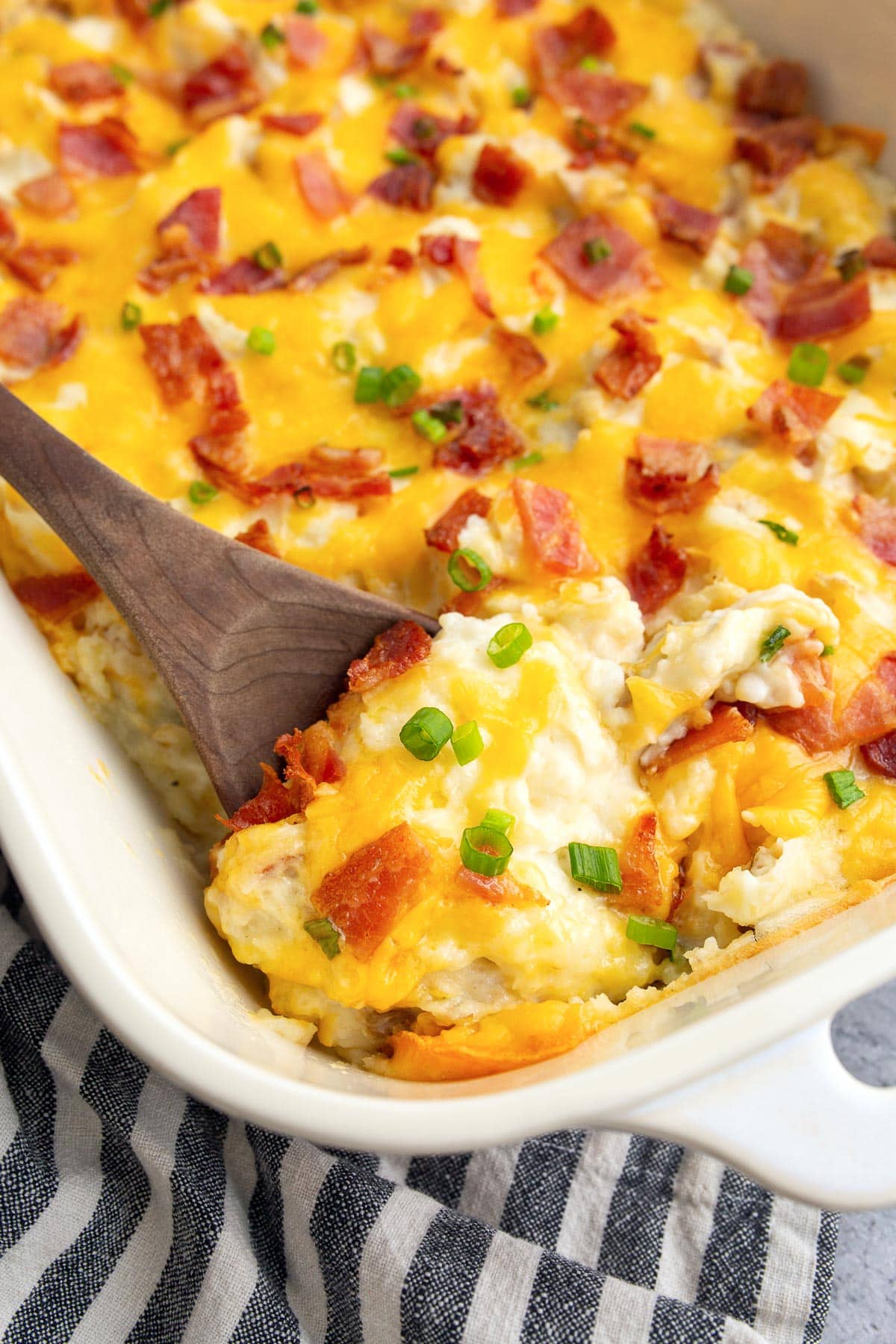 A close up shot of twice baked potato casserole topped with cheese, bacon bits and green onions.
