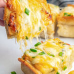 A slice of cheesy garlic bread torn in two with lots of cheese strings.