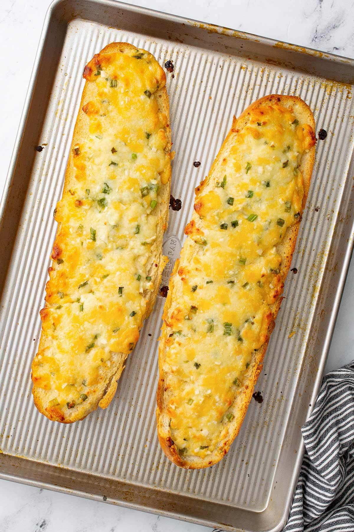 Two half loaves of freshly baked cheesy garlic bread on a baking sheet.