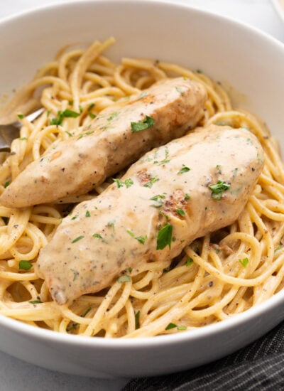 Two chicken tenders over a bed of spaghetti topped with lots of cream sauce and chopped fresh parsley.
