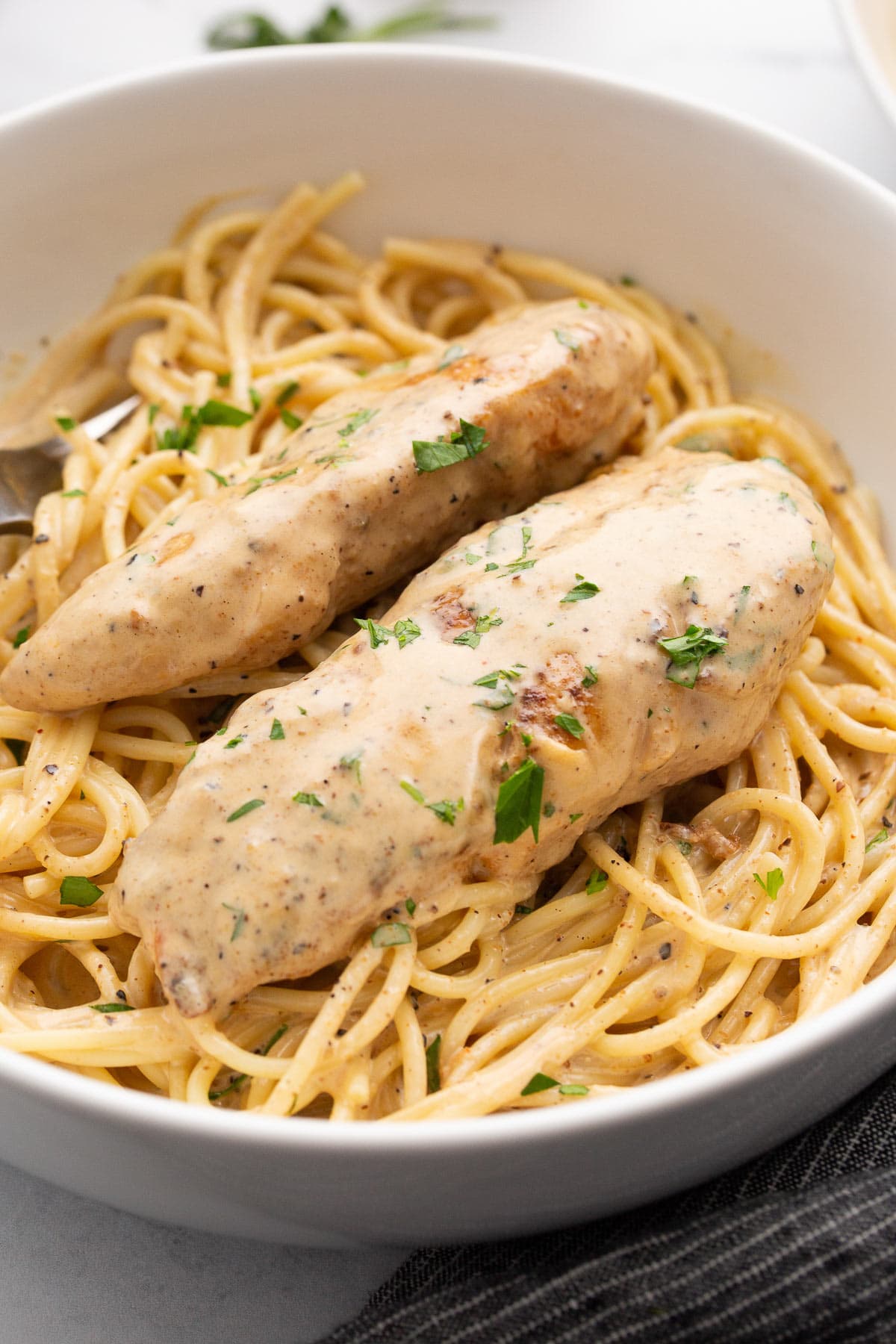 Two chicken tenders over a bed of spaghetti topped with lots of cream sauce and chopped fresh parsley.