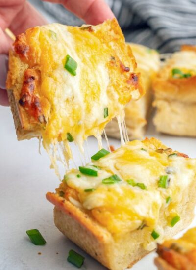 A slice of cheesy garlic bread torn in two with lots of cheese strings.