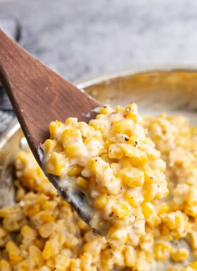 A generous serving of creamy honey butter skillet corn topped with freshly cracked black pepper on a wooden spoon.