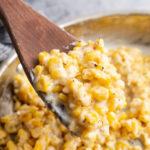 A generous serving of creamy honey butter skillet corn topped with freshly cracked black pepper on a wooden spoon.