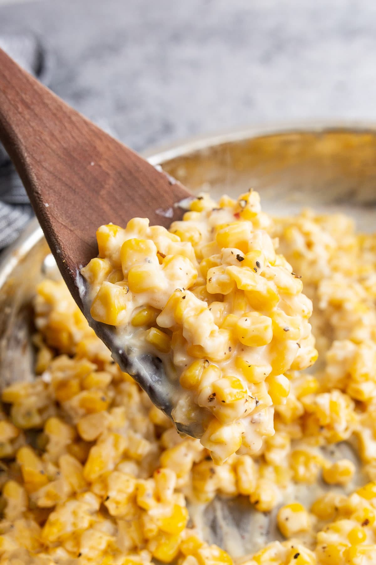 A generous serving of creamy honey butter skillet corn topped with freshly cracked black pepper on a wooden spoon.
