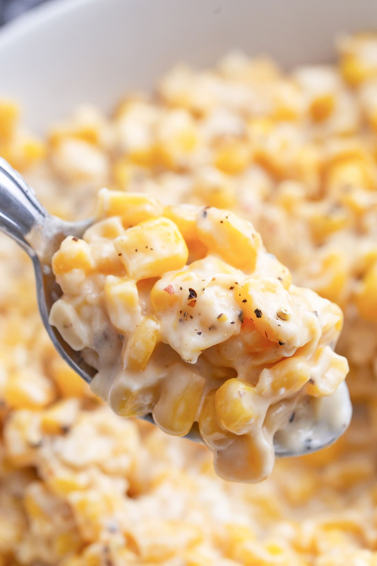 A generous serving of creamy honey butter skillet corn topped with freshly cracked black pepper on a spoon.