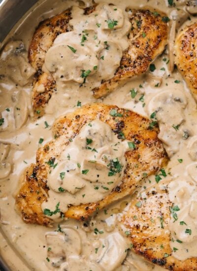Chicken with creamy mushroom sauce topped with fresh chopped parsley in a stainless steel skillet.