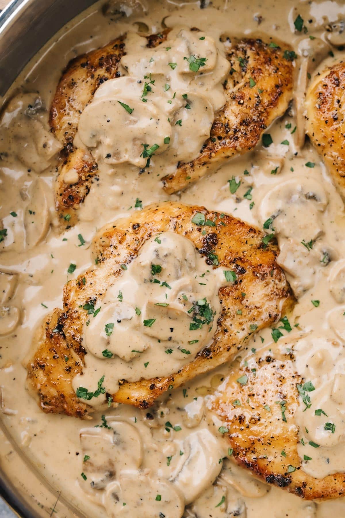 Chicken with creamy mushroom sauce topped with fresh chopped parsley in a stainless steel skillet.